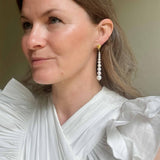 Woman wearing graduated pearl earrings with a white top against a neutral background