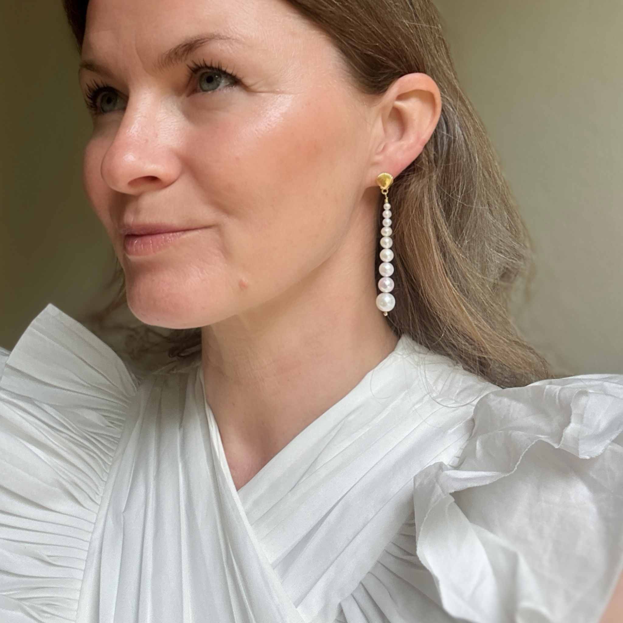 Woman wearing graduated pearl earrings with a white top against a neutral background