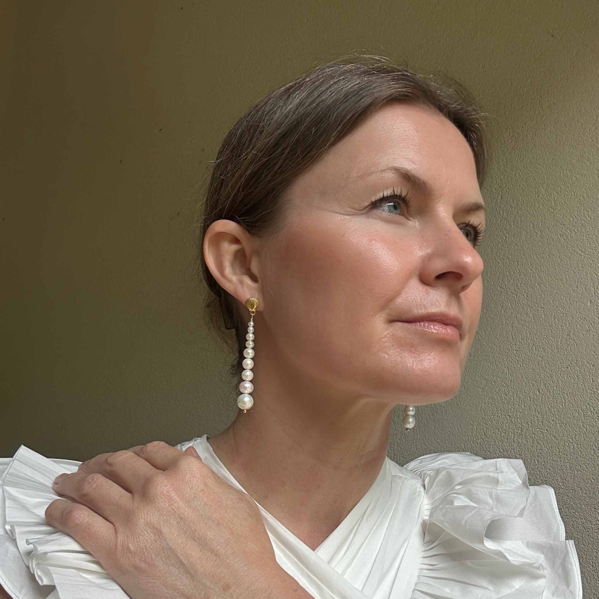 Woman wearing graduated freshwater pearl earrings against a plain background