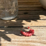 Pink beaded ring on a wooden surface with a glass jar in the background