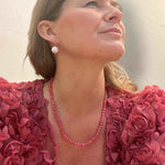 Woman wearing pearl earrings and a pink beaded necklace with a textured background