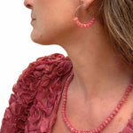 Close-up of a person wearing pink beaded earrings and a matching necklace against a white background