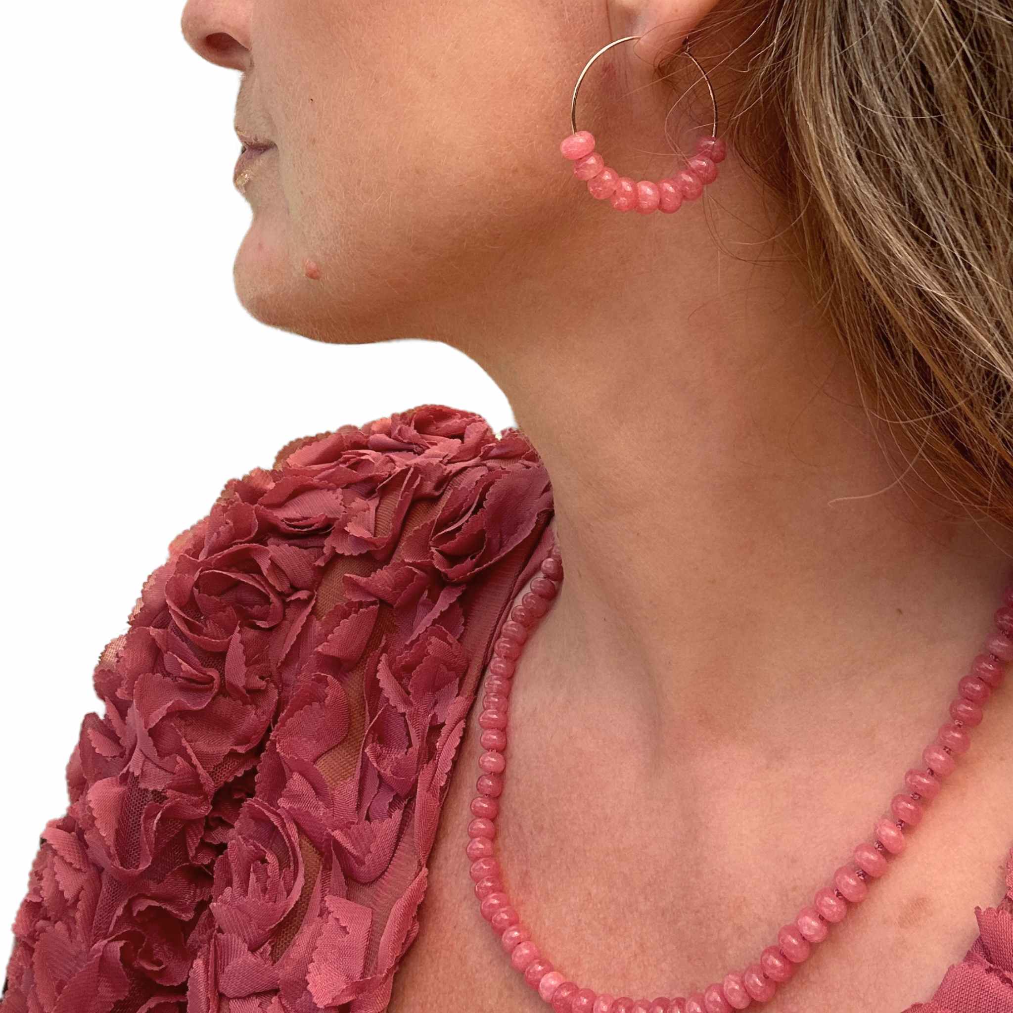Close-up of a person wearing pink beaded earrings and a matching necklace against a white background