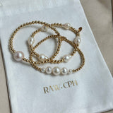 Gold bracelet with pearls on a white fabric with 'RAW.CPH' branding.