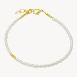 A white pearl bracelet with gold clasp and beads, laid out on a flat surface.